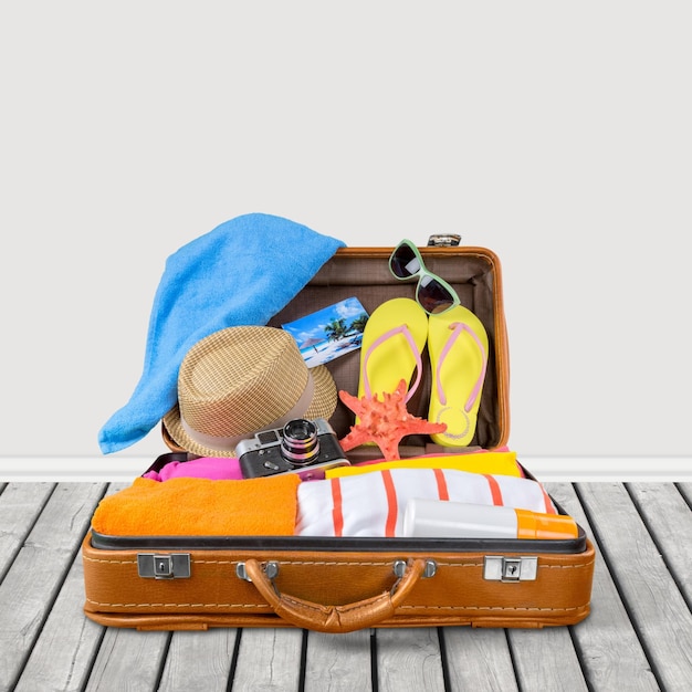 Foto maleta de viaje con sombrero de playa, chanclas y cámara retro en el fondo