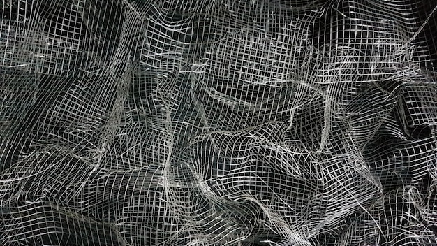 Malla arrugada. Fondo abstracto. Malla metálica con sombra sobre un fondo negro. La superficie de un rollo grande está dañada por una malla de alambre.