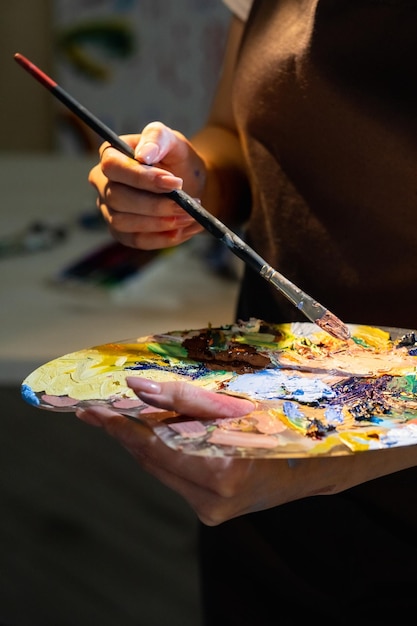 Malschule Weibliche Meisterklasse Künstlerisches Hobby Nicht erkennbare Frau, die eine Palette mit bunten Farben und Pinsel hält, bereit für die Erstellung von Kunstwerken im Studio-Interieur