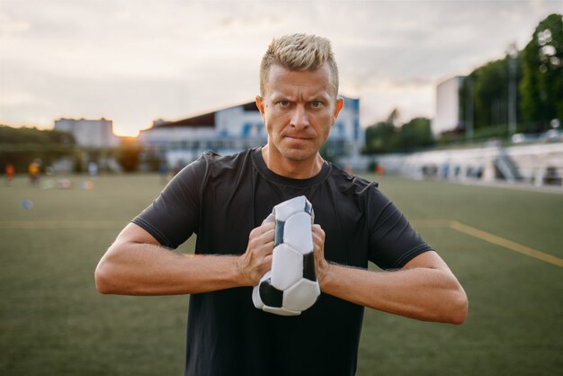 El malvado jugador de fútbol arrugó la pelota en el campo. Futbolista en el estadio al aire libre, entrenamiento antes del juego, entrenamiento de fútbol