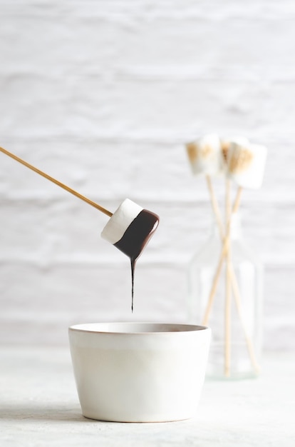 Un malvavisco blanco goteando chocolate y algunos malvaviscos en una botella, sobre fondo blanco.