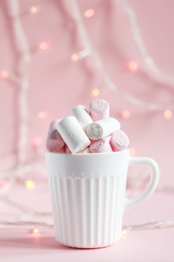 Foto malvaviscos blancos y rosas en una taza blanca sobre un fondo rosa. luces brillantes en el fondo