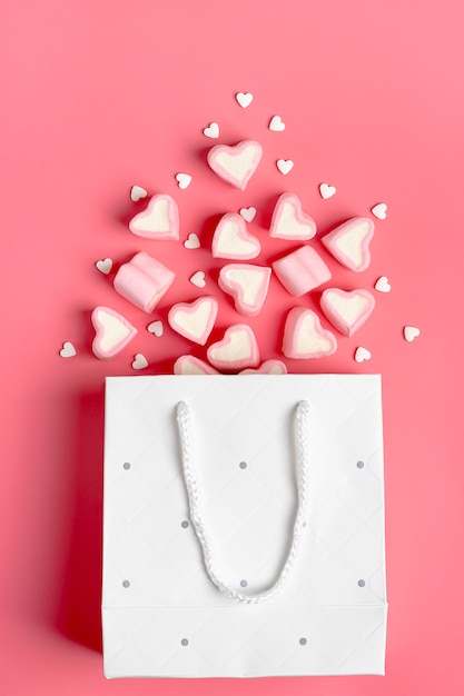 malvaviscos, caramelos en forma de corazón derramados de una bolsa de papel sobre fondo rosa Feliz Día de San Valentín