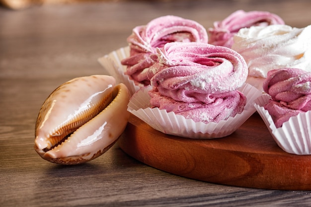 Malvaviscos de color rosa y blanco (céfiro) sobre una tabla redonda de madera con conchas marinas