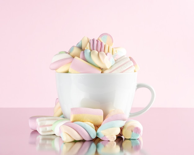 Malvaviscos coloridos caramelos masticables en una taza sobre fondo rosa