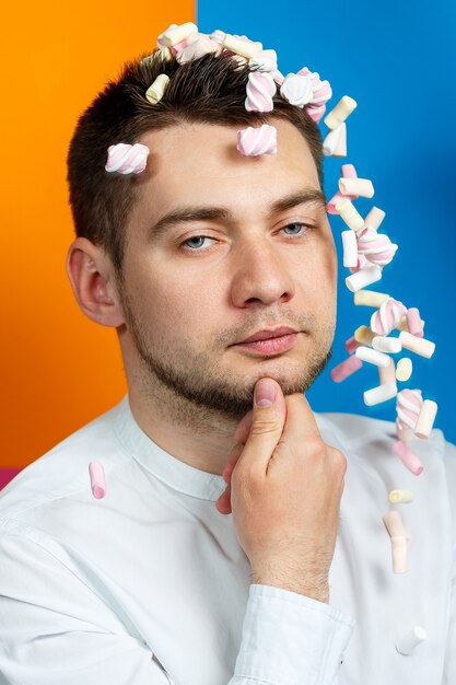 Los malvaviscos esparcen sobre la cabeza del hombre. Retrato de hombre brillante con dulces en el pelo