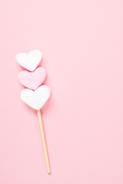 Malvaviscos en forma de corazón blanco y rosa en un palo de madera sobre un fondo de color rosa