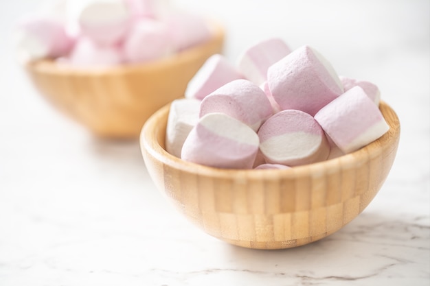 Malvaviscos rosados y blancos en cuencos de madera llenos colocados sobre una superficie de mármol con un enfoque en el cuenco en la parte delantera.