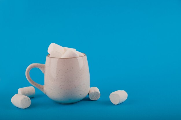 Malvaviscos en una taza en un espacio azul de cerca y copie el espacio. Marshmallow en una vista superior del patrón de taza en un espacio azul.