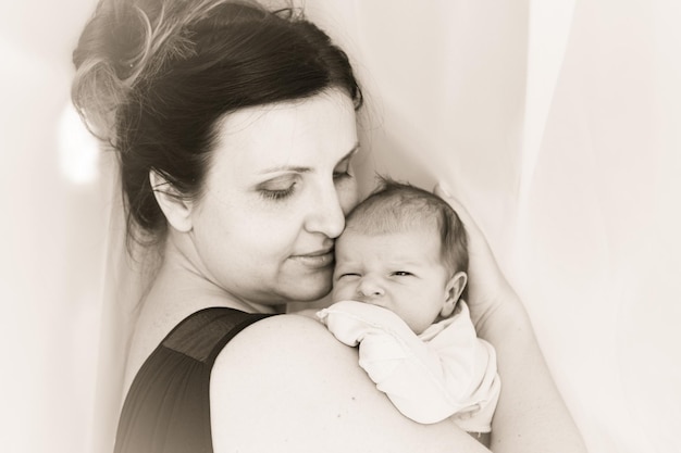 Mamá abraza a un bebé recién nacido. La madre sostiene al niño en las manos. En blanco y negro