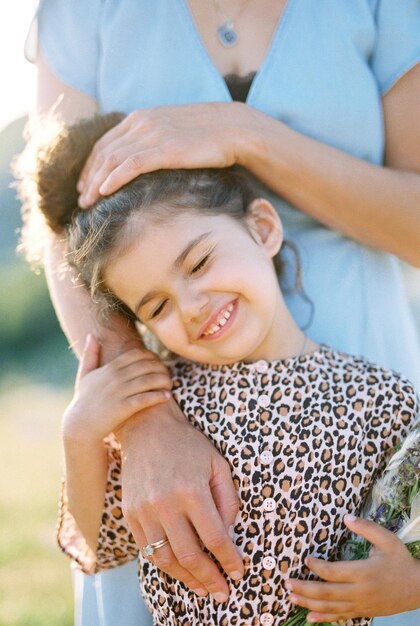 Mamá abraza a una niña poniendo su mano en su cabeza retrato recortado