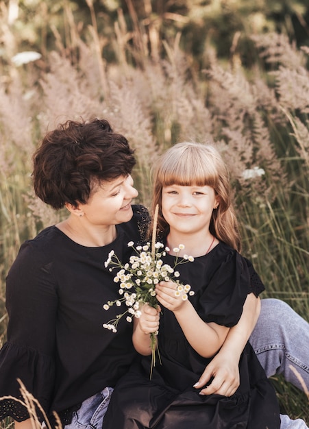 Mamá abraza suavemente a su hija en la naturaleza en el verano, feliz maternidad