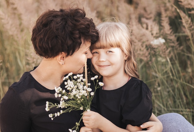 Mamá abraza suavemente a su hija en la naturaleza en el verano, feliz maternidad