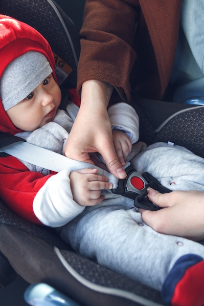 Mamá abrocha un cinturón de seguridad en el asiento del automóvil en el que se sienta su pequeño hijo