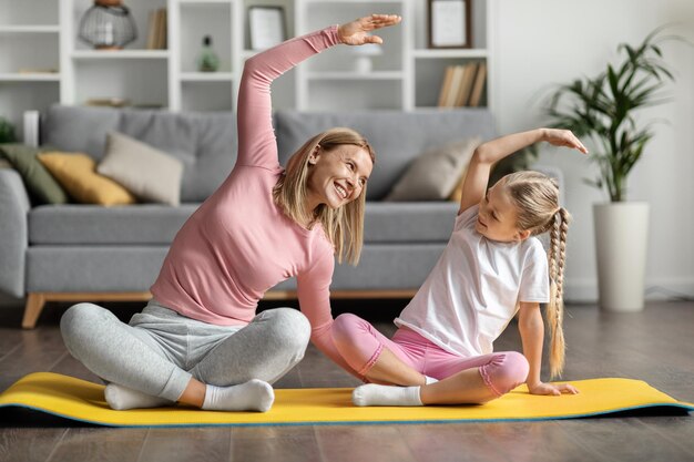 Foto mamá alegre y niña practicando yoga en casa juntas