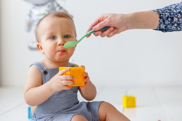 Mamá alimenta a un bebé de un año con una cuchara mientras juega con cubos Foto de alta calidad