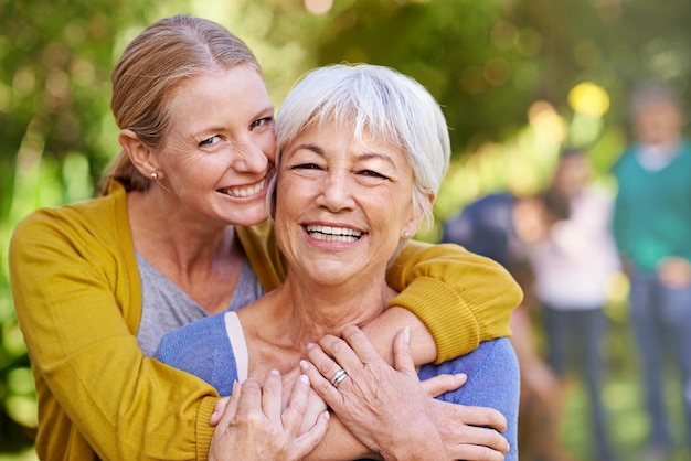 Mamá anciana y riendo con abrazo al aire libre por felicidad amor y cuidado en retrato de vacaciones Anciana mamá y abrazo con cara emocionada y familia en el patio trasero con sol de verano