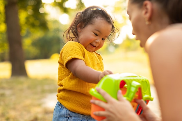 Mamá asiática dándole a su hija un juguete de plástico jugando al aire libre