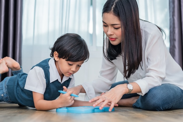 Mamá asiática enseñando a chico guapo a dibujar en la pizarra juntos