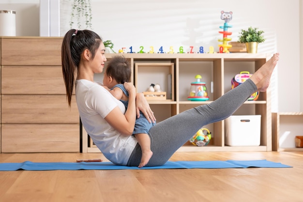 Foto mamá asiática jugando con un bebé adorable en la alfombra de yoga sonriendo y feliz en casa mamá hablando con el bebé divirtiéndose y riendo vomitando a su hijo en el aire haciendo ejercicio juntos tiempo de relajaciónbaby y día de la madre