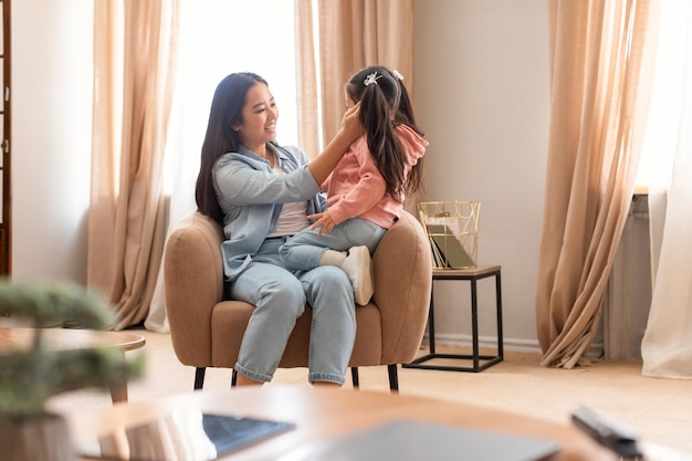 Mamá asiática y su pequeña hija sentadas en un sillón en casa