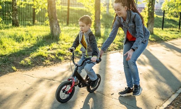 Mamá ayuda a un niño a aprender a andar en bicicleta de dos ruedas en el parque Unas agradables vacaciones deportivas de verano para niños