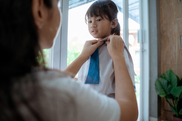 Mamá ayuda a ponerse el uniforme de su hija antes de la escuela