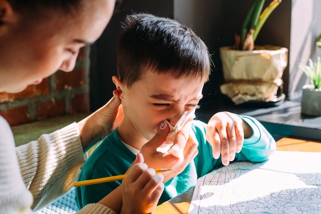 Mamá ayuda a su pequeño hijo a sonarse la nariz con un concepto de alergia a la servilleta