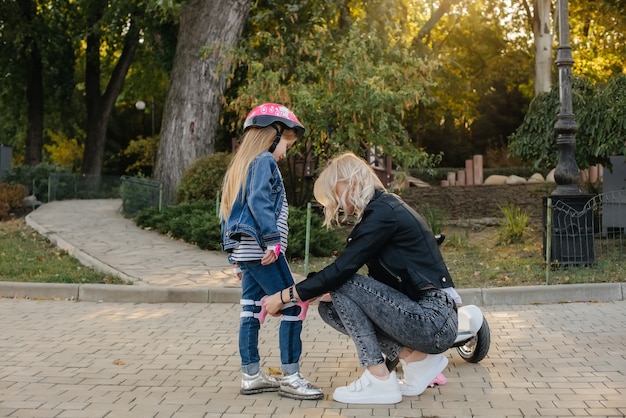 Mamá ayuda a vestir el equipo y el casco de su pequeña hija para un paseo en Segway por el parque