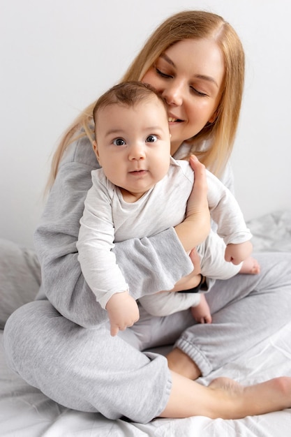 Mamá y bebé juegan en la cama Madre e hijo familia feliz hermosa niña rubia y lindo bebé en casa