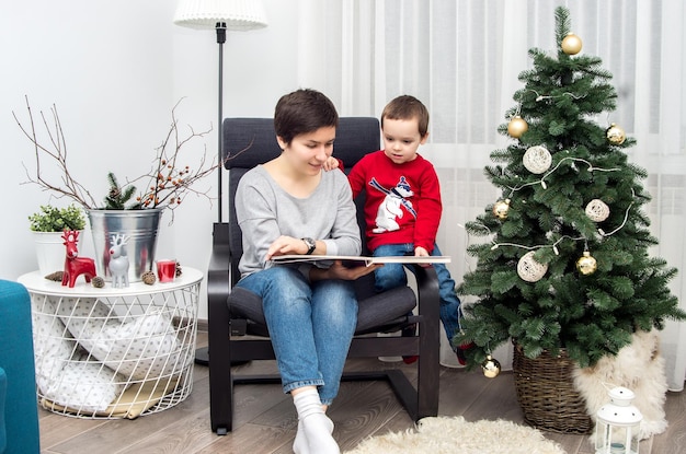 Mamá y bebé leyendo un libro en la habitación en Nochebuena