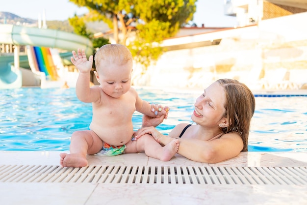 Mamá y bebé en la piscina con toboganes de agua en verano se divierten nadando relajándose y pasando tiempo con la familia de vacaciones