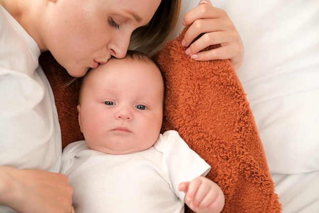 Mamá con un bebé recién nacido yace en la cama madre besa el amor de la madre del niño