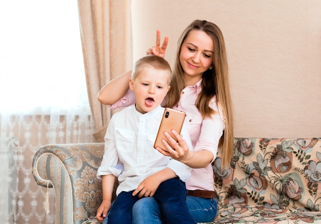 Mamá y bebé tomando un selfie en una acogedora sala de estar. mamá e hijo hacen muecas y se toman fotos en la cámara