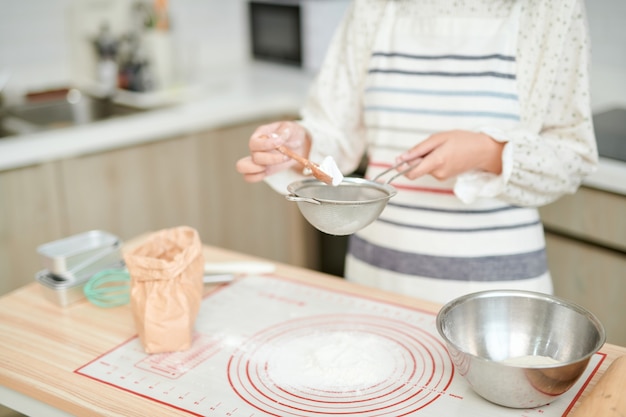 Mama bereitet das Frühstück zu. Eine Frau gießt Mehl in einen Teller. Der Kochvorgang. Küche zu Hause