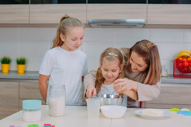 Mama bringt ihren Töchtern bei, in der Küche Teig zu kochen.