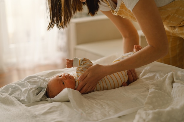 Mamá cambiando su pañal bebé recién nacido. Feliz joven madre jugando con el bebé mientras le cambia el pañal en la cama. Feliz maternidad