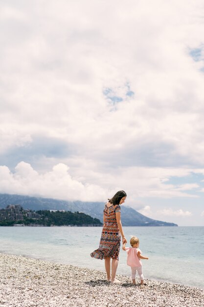 Mamá camina con una niña en una playa de guijarros