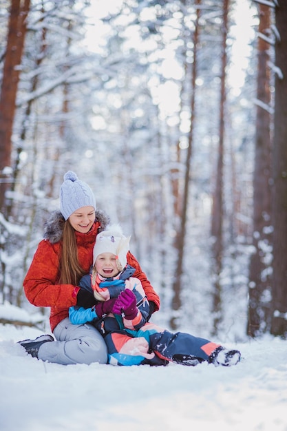 Mamá camina con su hija en un bosque nevado Paseo en trineos abrazados