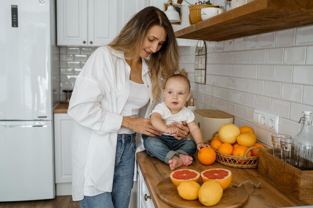 mamá con una camisa blanca corta fruta para el desayuno junto a su hijo en una cocina blanca