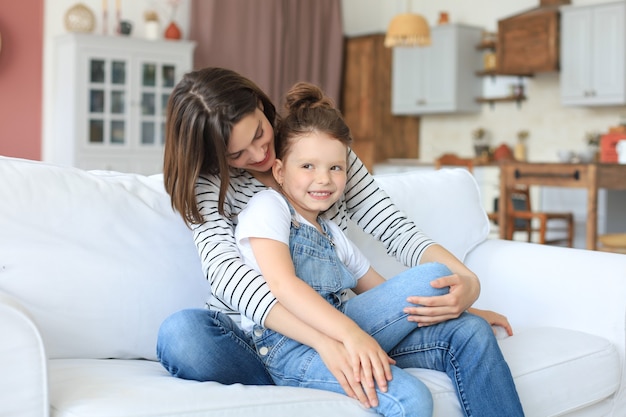 Mamá cariñosa feliz abrazando a la pequeña hija, pasar tiempo juntos en casa.