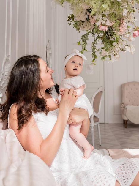 Mamá caucásica está sentada en la cama con una niña y abrazando a una tierna foto de mamá y bebé en el interior