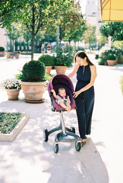 Mamá se para cerca del cochecito con el bebé en la calle cerca de las macetas