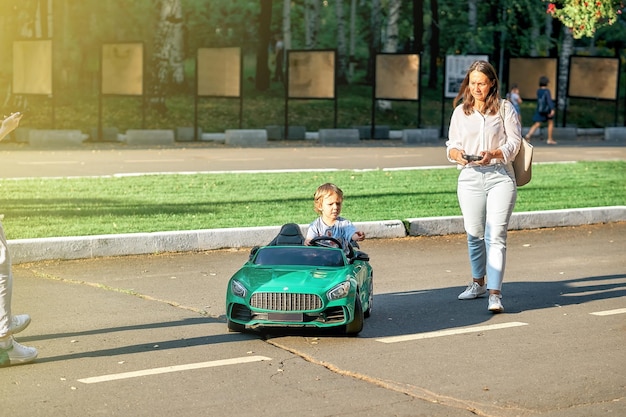 Mamá controla el coche de los niños con control remoto al caminar con un niño pequeño en un parque público