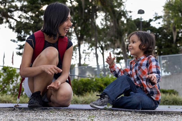 Mamá conversa y con su pequeño hijo latinoamericano mientras ambos se divierten y juegan en un parque infantil Concepto y enseñanza del día de la madre