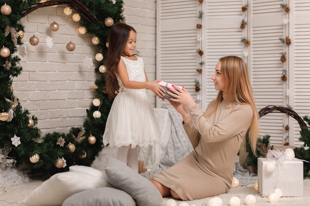 Mamá le da caja de regalo a una linda niña para Navidad en casa