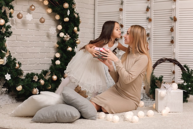 Mamá le da caja de regalo a una linda niña para Navidad en casa