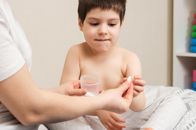 Mamá le da una pastilla al niño que trata a los niños en casa.