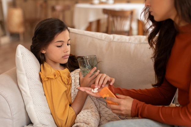 Mamá le da una pastilla de antibióticos a su hija enferma en casa