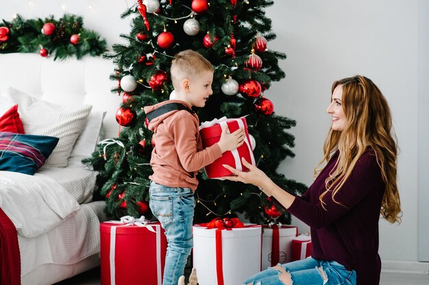 Mamá le da a su hijo un regalo cerca del árbol de Navidad